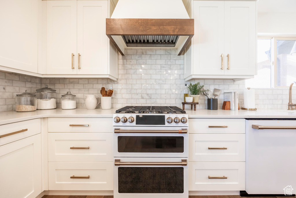 Kitchen with premium range hood, backsplash, white appliances, and white cabinets