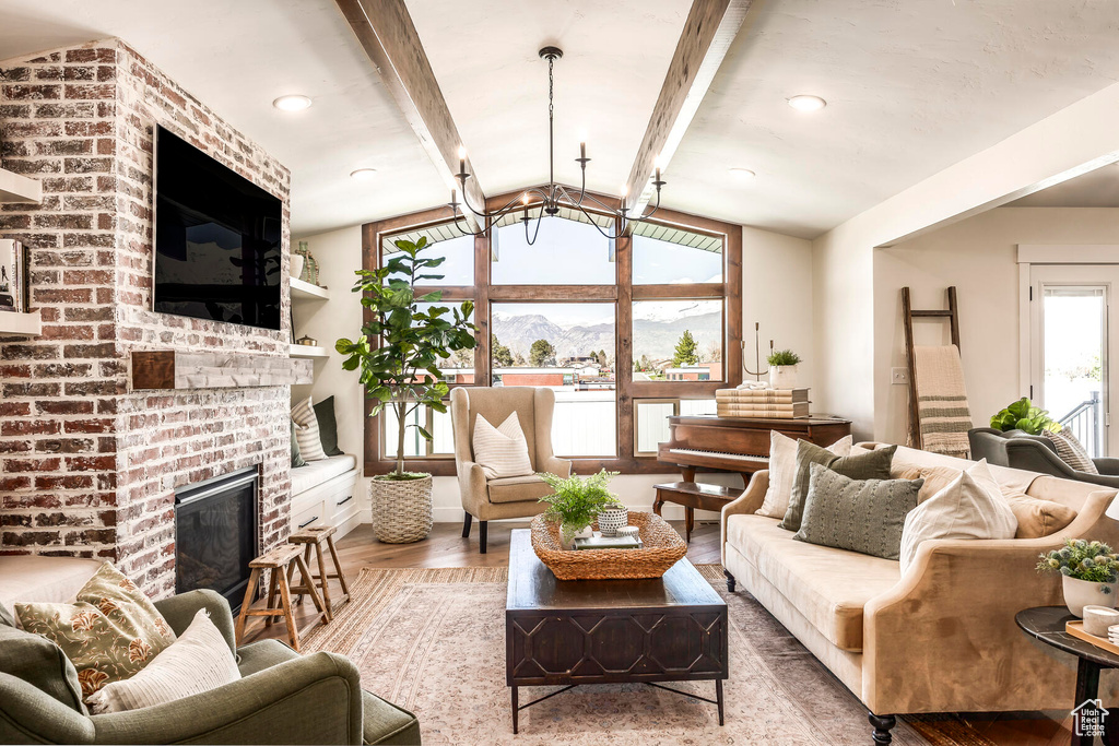 Living room featuring lofted ceiling with beams, brick wall, light wood-type flooring, and a fireplace