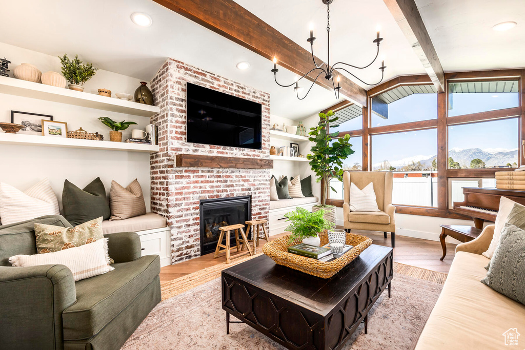 Living room featuring light wood-type flooring, a brick fireplace, a mountain view, brick wall, and lofted ceiling with beams