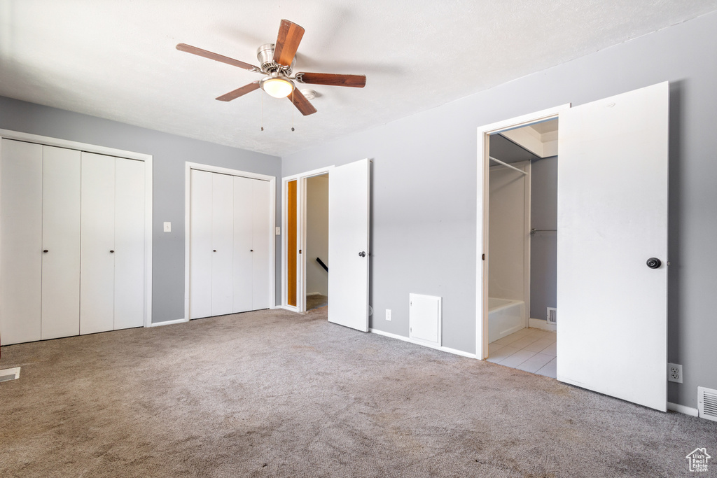 Unfurnished bedroom with multiple closets, light carpet, ceiling fan, and ensuite bathroom