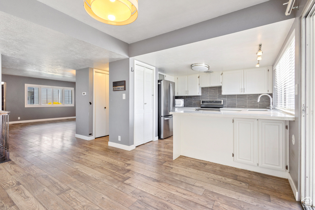 Kitchen featuring white cabinets, tasteful backsplash, light wood-type flooring, and stainless steel fridge