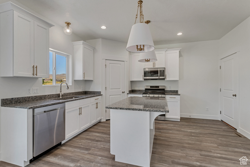 Kitchen with white cabinets, appliances with stainless steel finishes, sink, hardwood / wood-style flooring, and decorative light fixtures