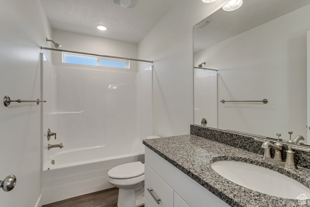 Full bathroom with shower / tub combination, toilet, hardwood / wood-style flooring, and vanity with extensive cabinet space