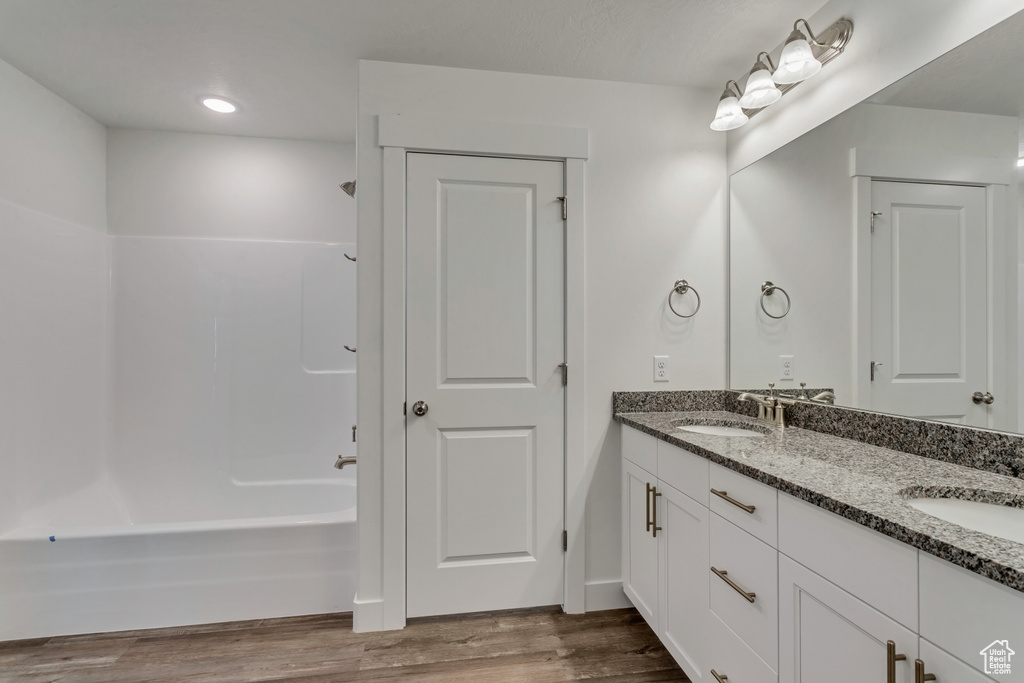 Bathroom featuring vanity with extensive cabinet space, dual sinks, washtub / shower combination, and wood-type flooring