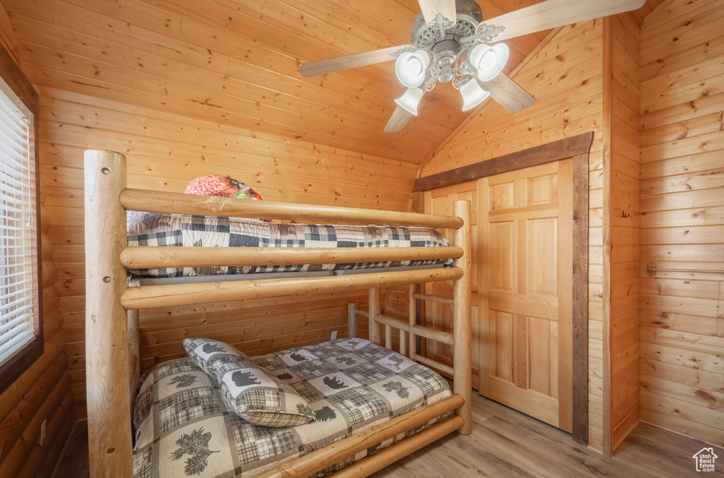 Bedroom with lofted ceiling, hardwood / wood-style floors, ceiling fan, and wooden walls