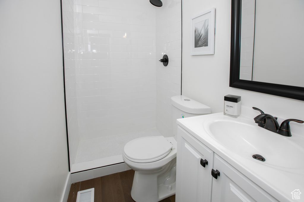Bathroom with oversized vanity, tiled shower, toilet, and hardwood / wood-style flooring