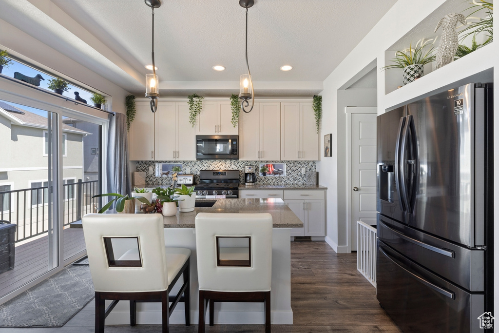 Kitchen featuring backsplash, stainless steel appliances, dark hardwood / wood-style floors, white cabinets, and pendant lighting