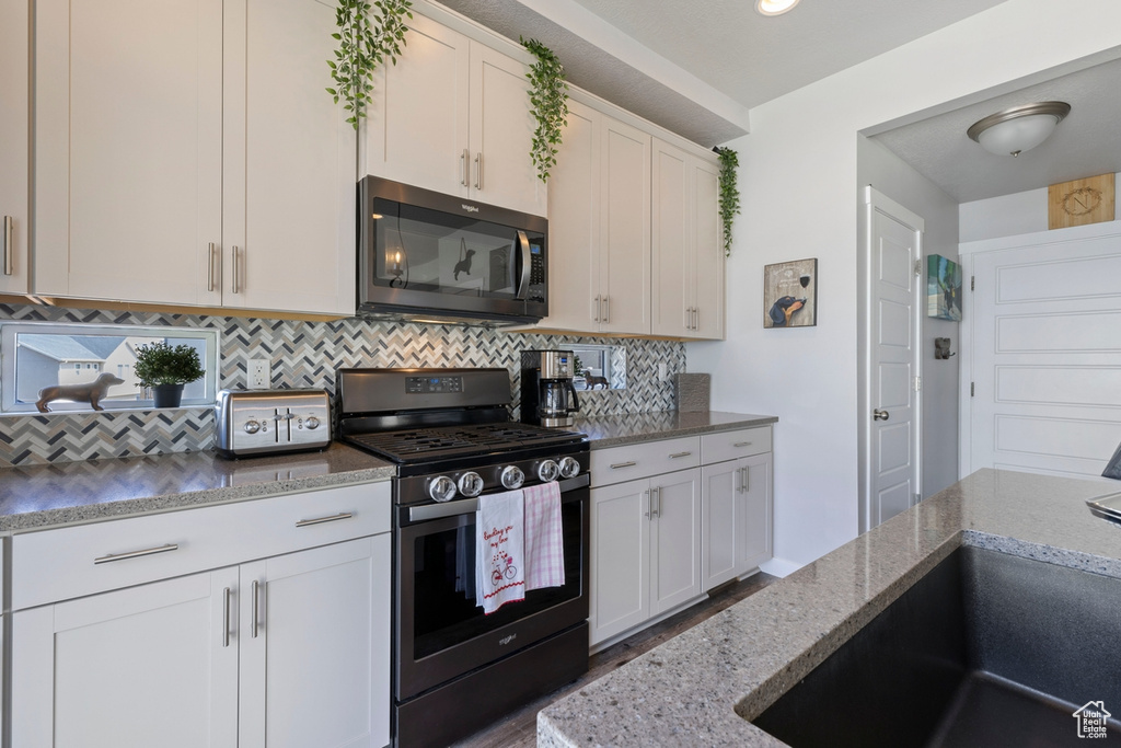 Kitchen featuring backsplash, dark stone counters, gas range, white cabinetry, and sink