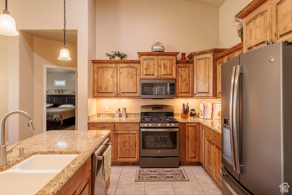 Kitchen with light tile floors, sink, hanging light fixtures, stainless steel appliances, and light stone countertops