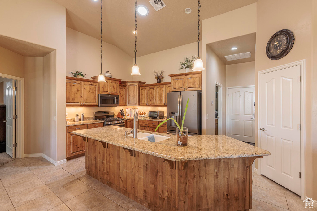 Kitchen featuring light stone countertops, decorative light fixtures, stainless steel appliances, a center island with sink, and sink