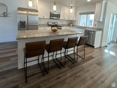 Kitchen featuring decorative light fixtures, dark hardwood / wood-style flooring, white cabinetry, appliances with stainless steel finishes, and a kitchen island