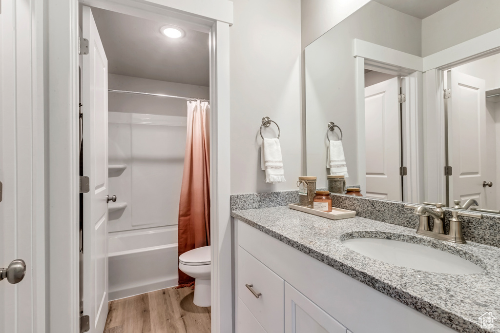 Full bathroom with hardwood / wood-style floors, oversized vanity, toilet, and shower / bath combo with shower curtain
