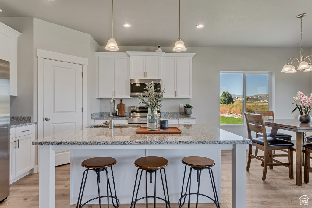 Kitchen featuring hanging light fixtures, light stone countertops, white cabinetry, appliances with stainless steel finishes, and light hardwood / wood-style floors