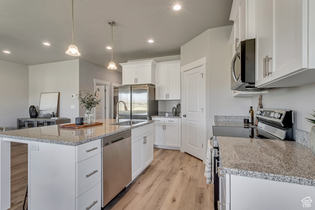 Kitchen with appliances with stainless steel finishes, light hardwood / wood-style flooring, hanging light fixtures, a center island with sink, and white cabinets