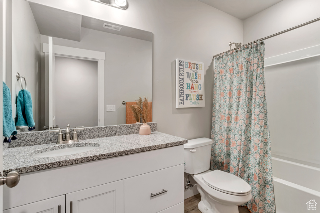 Full bathroom featuring oversized vanity, shower / bathtub combination with curtain, and toilet