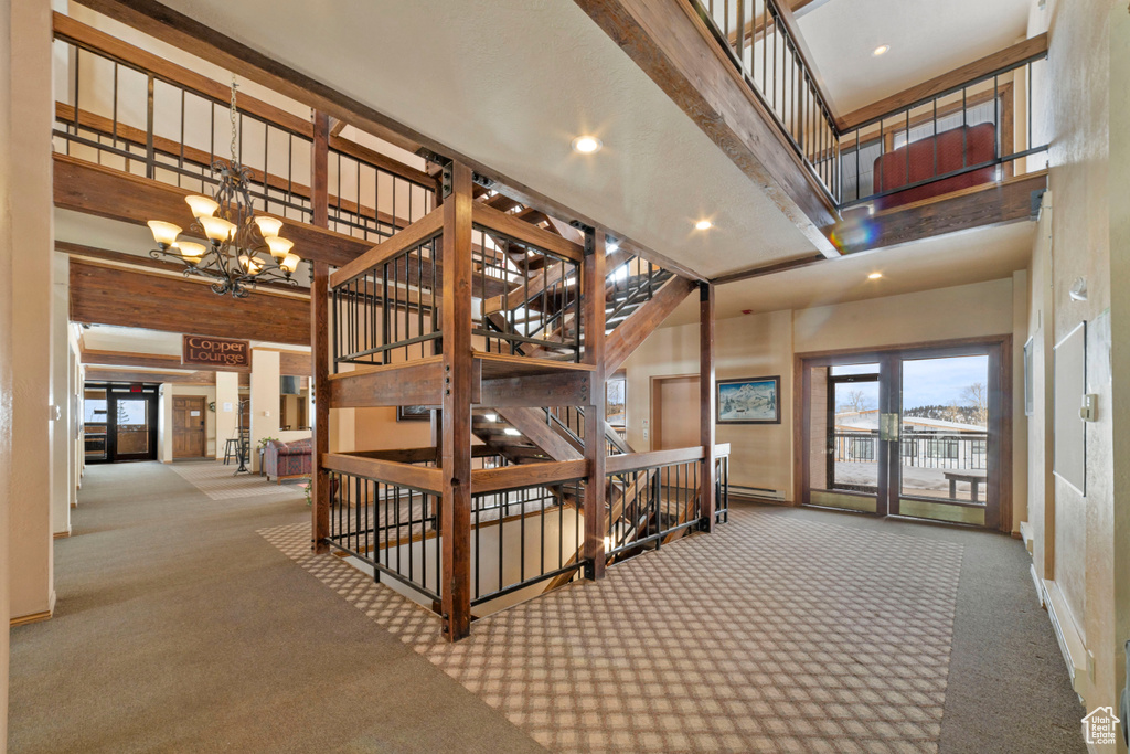 Stairs with an inviting chandelier, light colored carpet, baseboard heating, and a high ceiling