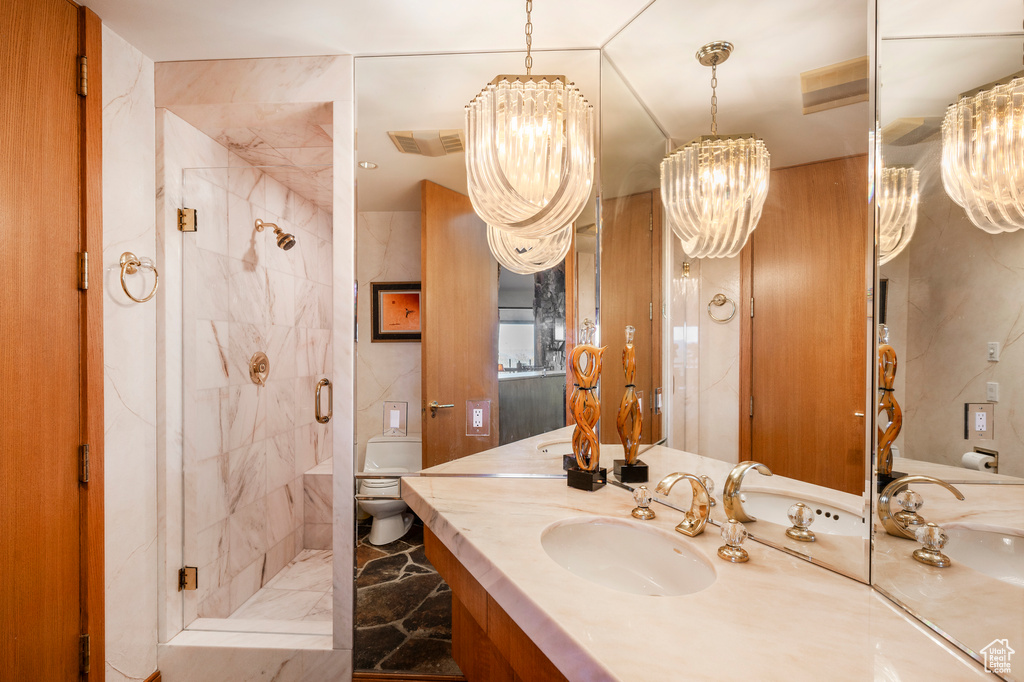 Bathroom with tiled shower, vanity with extensive cabinet space, toilet, and a notable chandelier