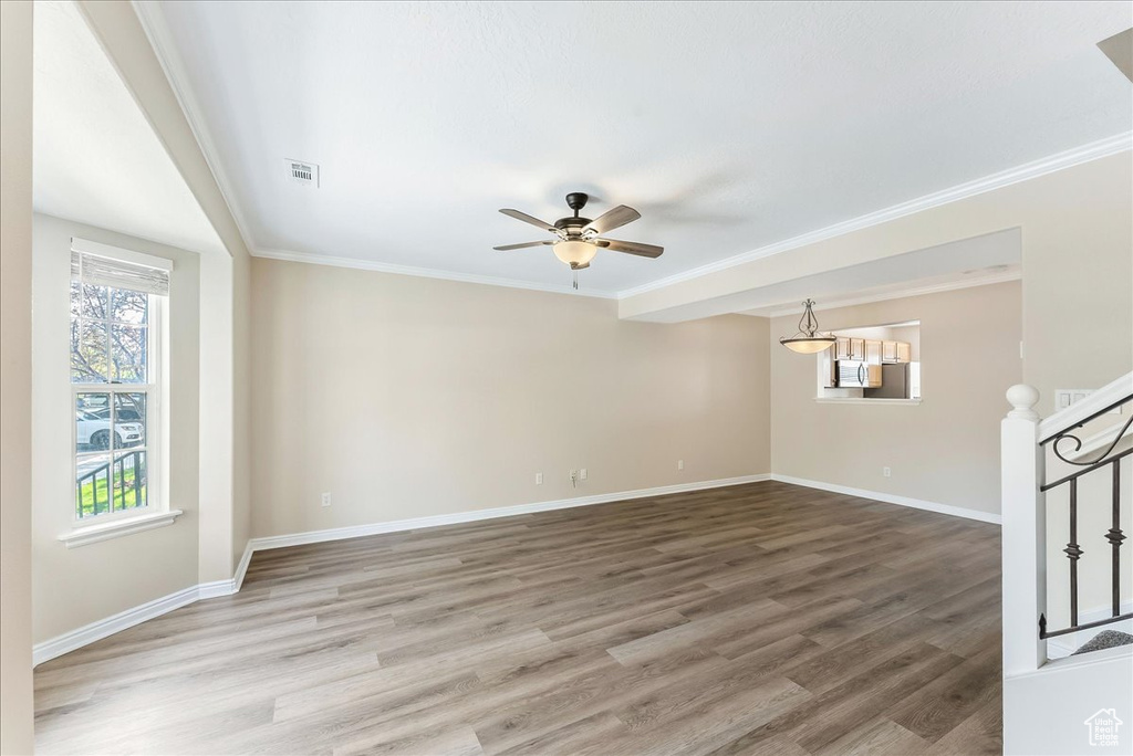 Empty room with ceiling fan, crown molding, and light wood-type flooring
