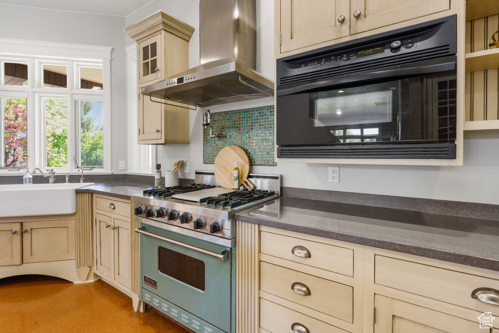 Kitchen featuring wall chimney exhaust hood, oven, sink, tasteful backsplash, and luxury range
