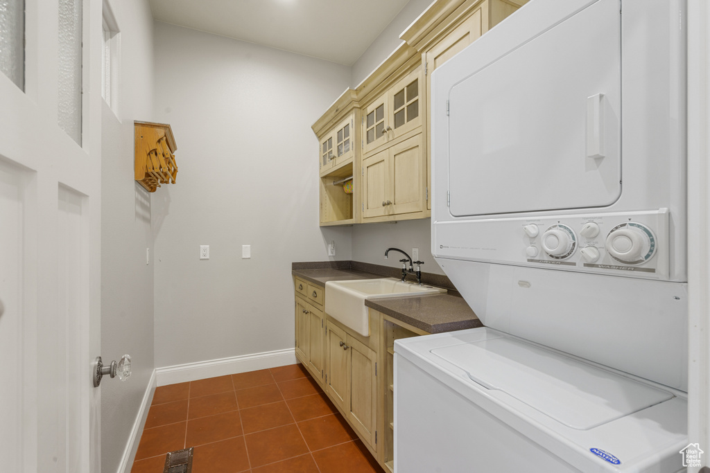 Laundry room featuring cabinets, dark tile flooring, stacked washer and dryer, and sink