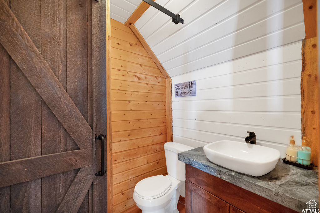 Bathroom with wooden walls, toilet, vanity, and lofted ceiling