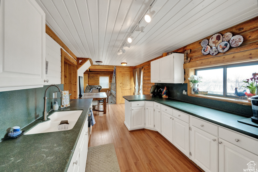 Kitchen with wood walls, white cabinets, rail lighting, light wood-type flooring, and sink