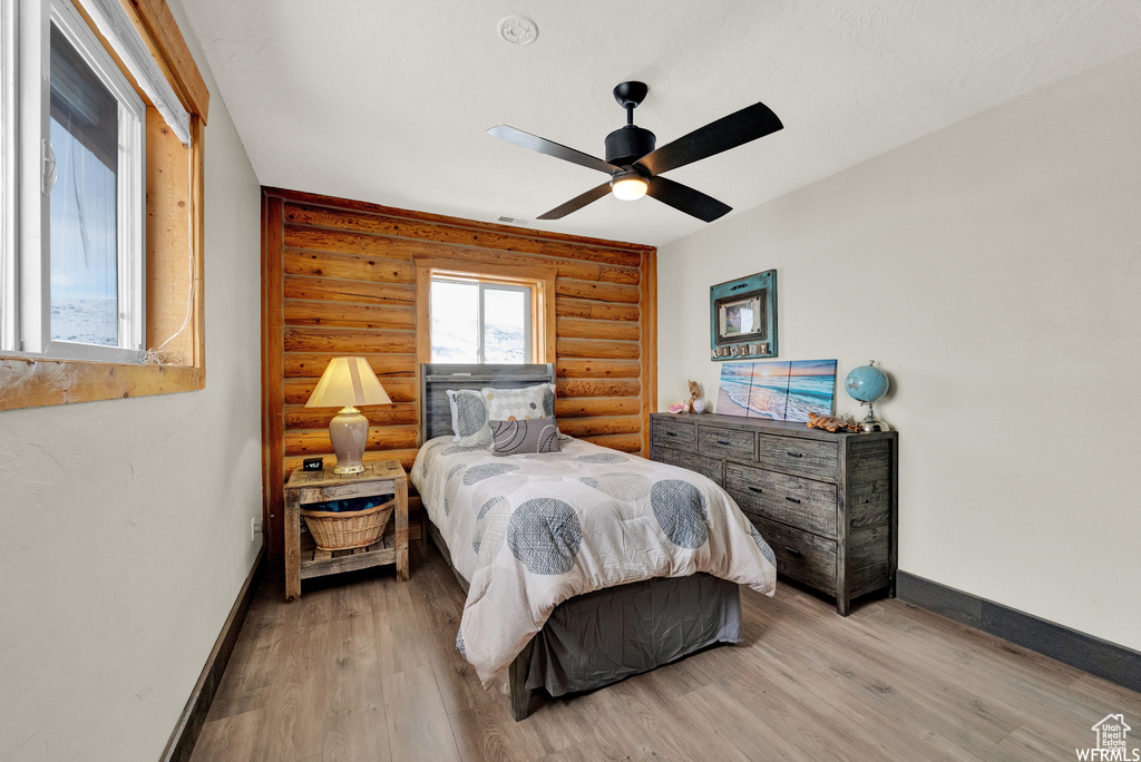 Bedroom featuring ceiling fan, light wood-type flooring, and rustic walls