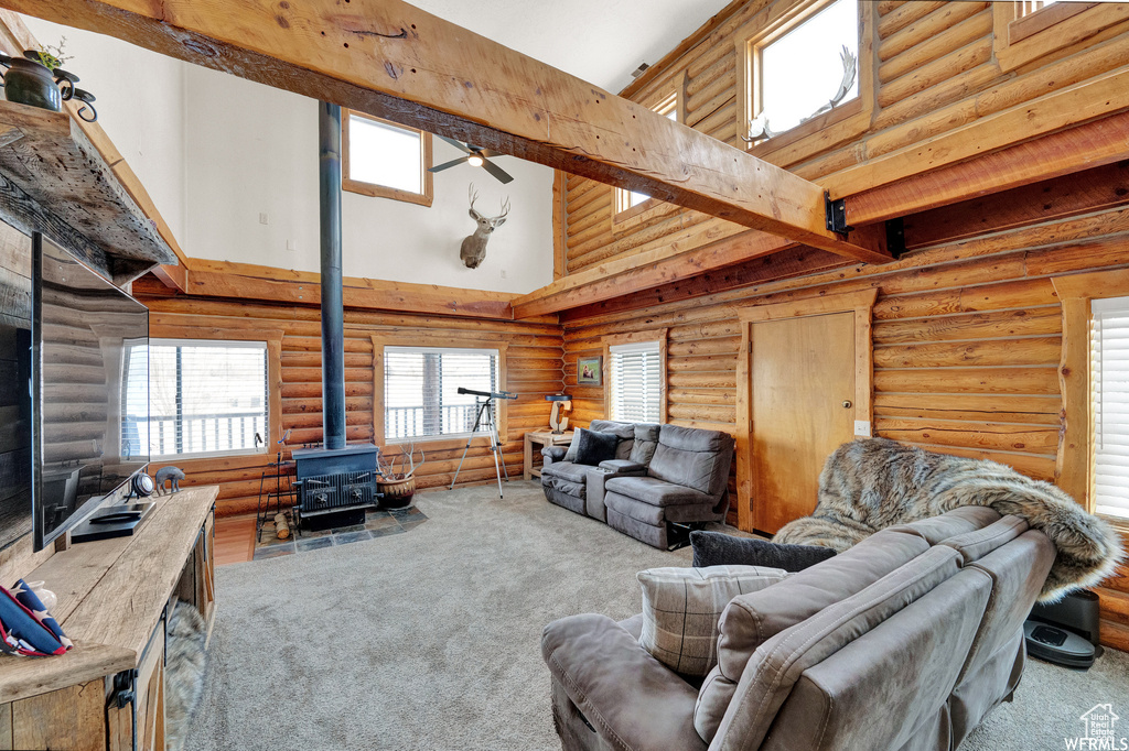 Carpeted living room featuring a wood stove, beam ceiling, a high ceiling, and rustic walls