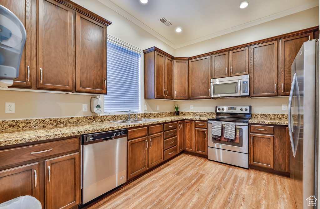 Kitchen featuring light stone countertops, ornamental molding, appliances with stainless steel finishes, sink, and light hardwood / wood-style floors