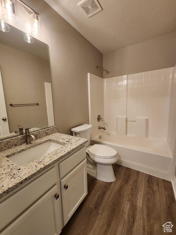 Full bathroom with wood-type flooring, shower / bathing tub combination, vanity, toilet, and a textured ceiling