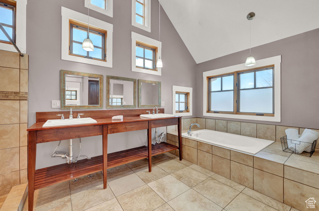 Bathroom with high vaulted ceiling, oversized vanity, tile flooring, dual sinks, and tiled bath