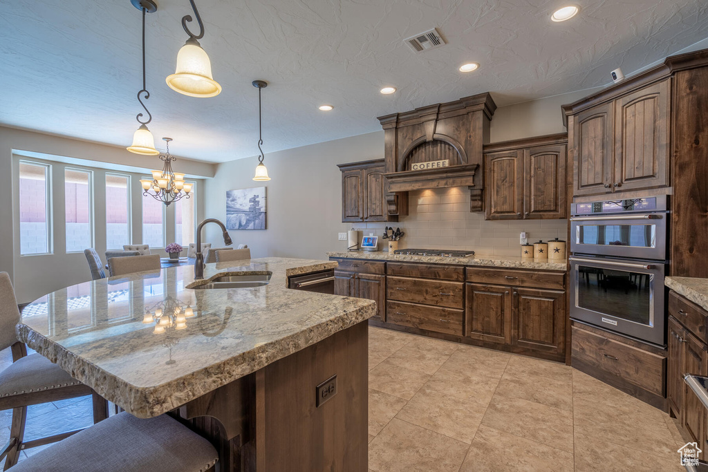 Kitchen with a kitchen breakfast bar, pendant lighting, stainless steel appliances, sink, and an island with sink