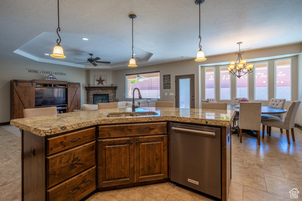 Kitchen with a fireplace, sink, a raised ceiling, stainless steel dishwasher, and decorative light fixtures