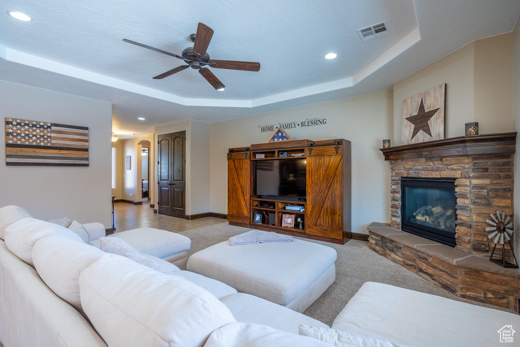 Carpeted living room with a barn door, ceiling fan, a raised ceiling, and a fireplace