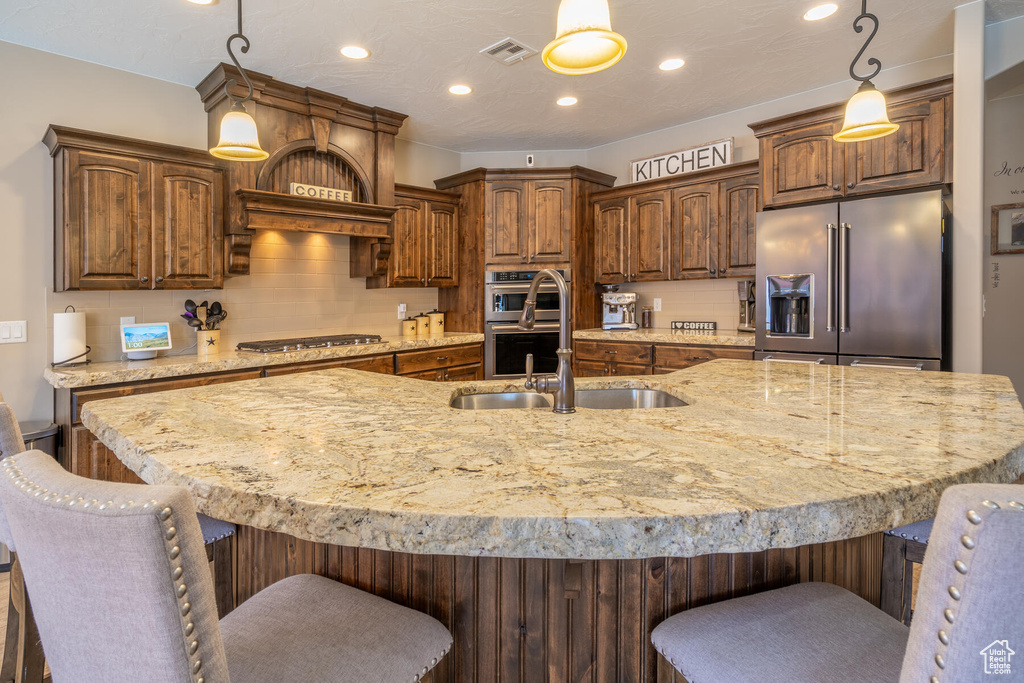 Kitchen with hanging light fixtures, a large island with sink, stainless steel appliances, and a breakfast bar