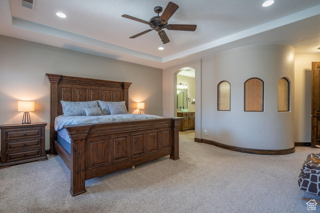Bedroom featuring connected bathroom, light carpet, ceiling fan, and a tray ceiling