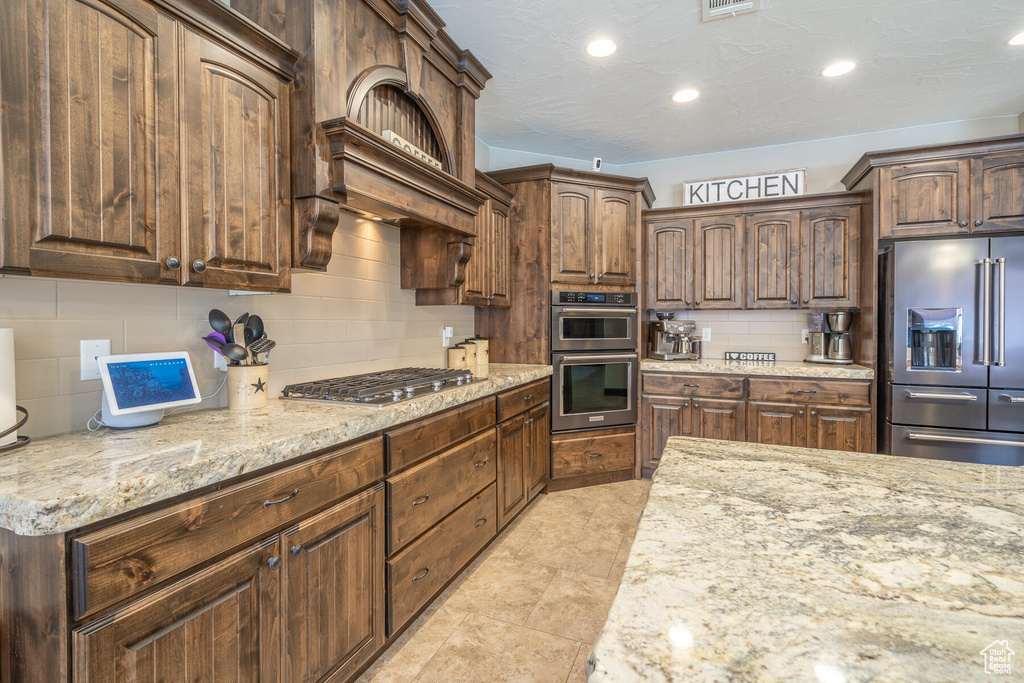 Kitchen with appliances with stainless steel finishes, dark brown cabinetry, backsplash, and light tile floors