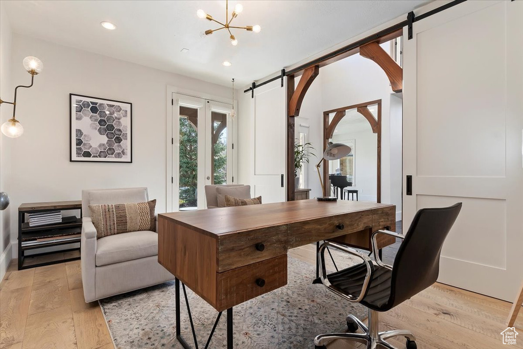 Office space with light hardwood / wood-style flooring, an inviting chandelier, and a barn door