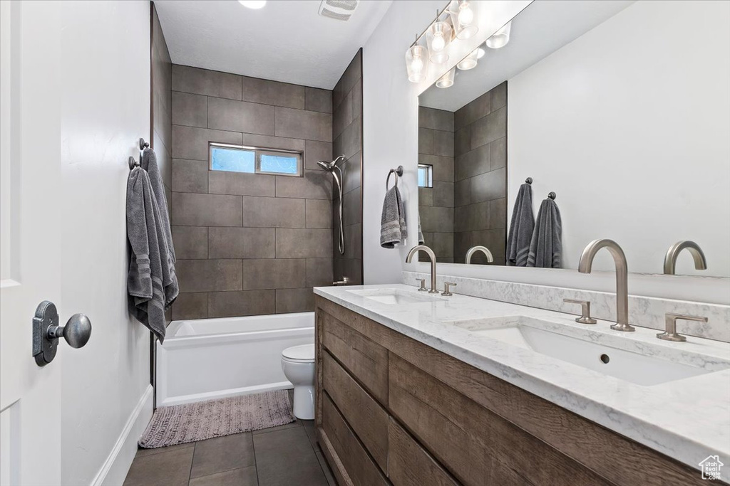Full bathroom featuring tiled shower / bath, large vanity, double sink, tile floors, and toilet