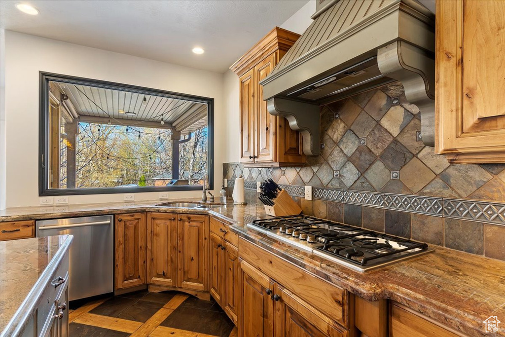 Kitchen featuring appliances with stainless steel finishes, premium range hood, tasteful backsplash, dark tile flooring, and sink