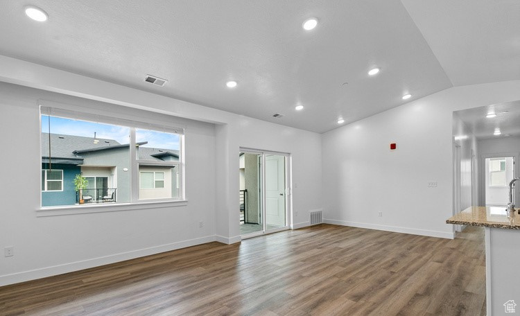 Empty room featuring hardwood / wood-style flooring, plenty of natural light, and lofted ceiling