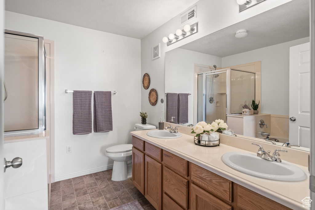 Bathroom with an enclosed shower, dual bowl vanity, toilet, and tile flooring
