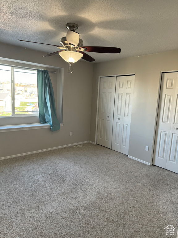 Unfurnished bedroom featuring light carpet, ceiling fan, and multiple closets