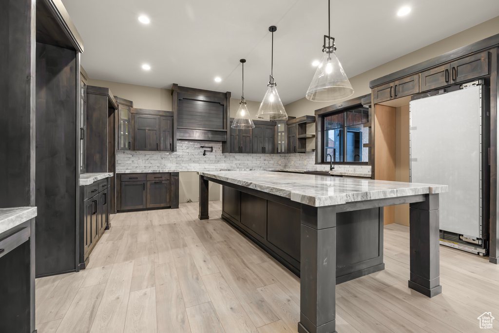 Kitchen with a kitchen island, a breakfast bar area, tasteful backsplash, pendant lighting, and light wood-type flooring
