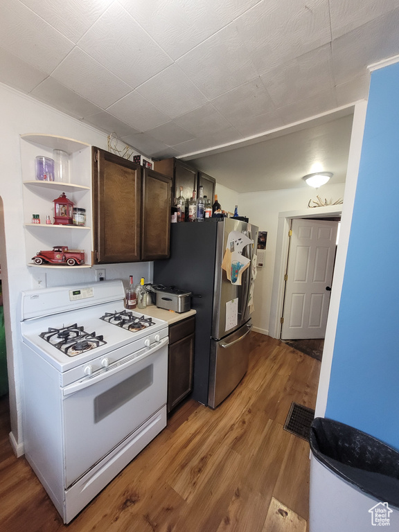 Kitchen with hardwood / wood-style floors, dark brown cabinets, stainless steel refrigerator, and white gas stove