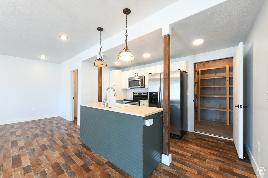Kitchen with appliances with stainless steel finishes, dark wood-type flooring, white cabinets, sink, and pendant lighting