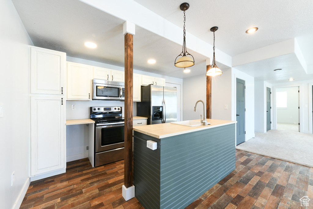 Kitchen featuring appliances with stainless steel finishes, white cabinets, sink, hanging light fixtures, and dark hardwood / wood-style floors