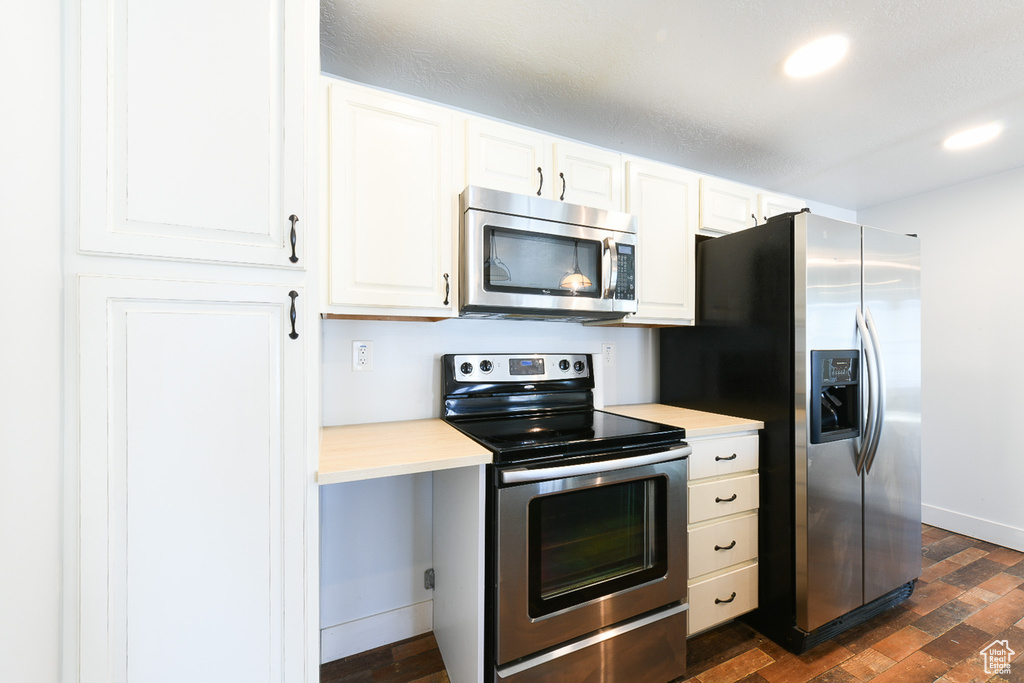 Kitchen with appliances with stainless steel finishes, dark hardwood / wood-style flooring, and white cabinets