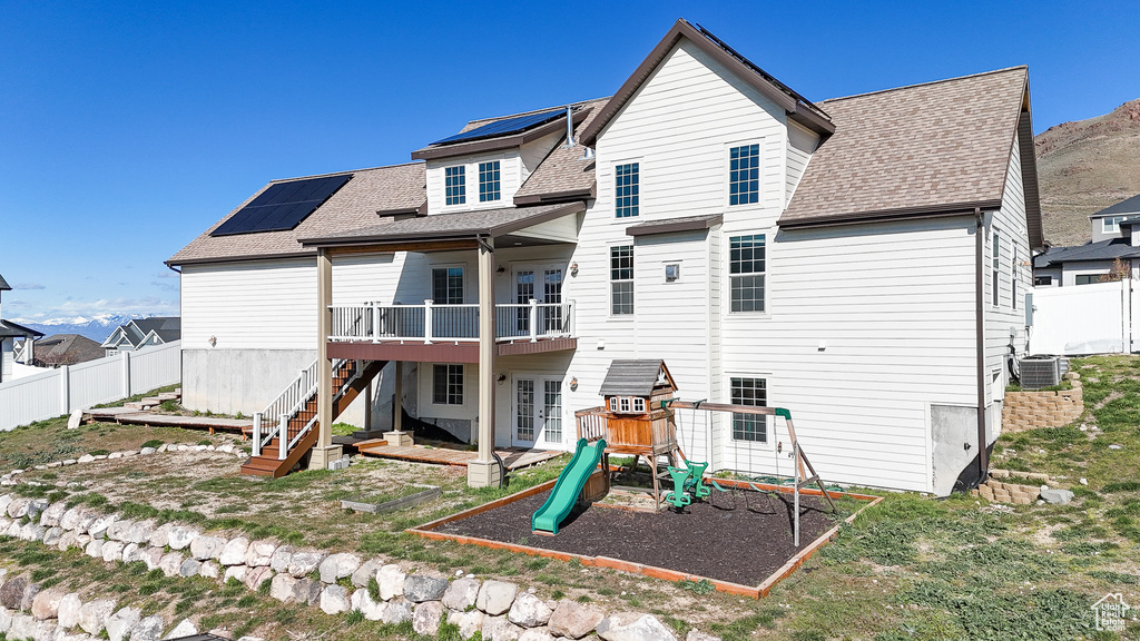 Back of property with solar panels, a yard, a playground, and central AC