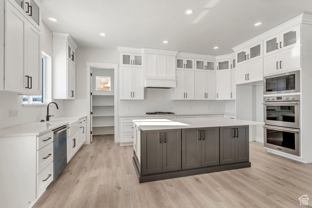 Kitchen featuring a kitchen island, appliances with stainless steel finishes, white cabinets, and light wood-type flooring